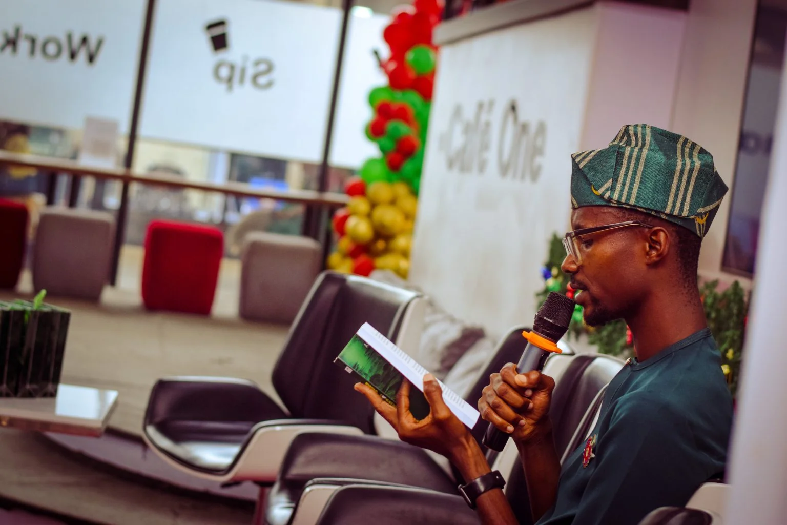 Ajíbọ́lá Ọládìípọ̀ reading from a book while speaking into a microphone